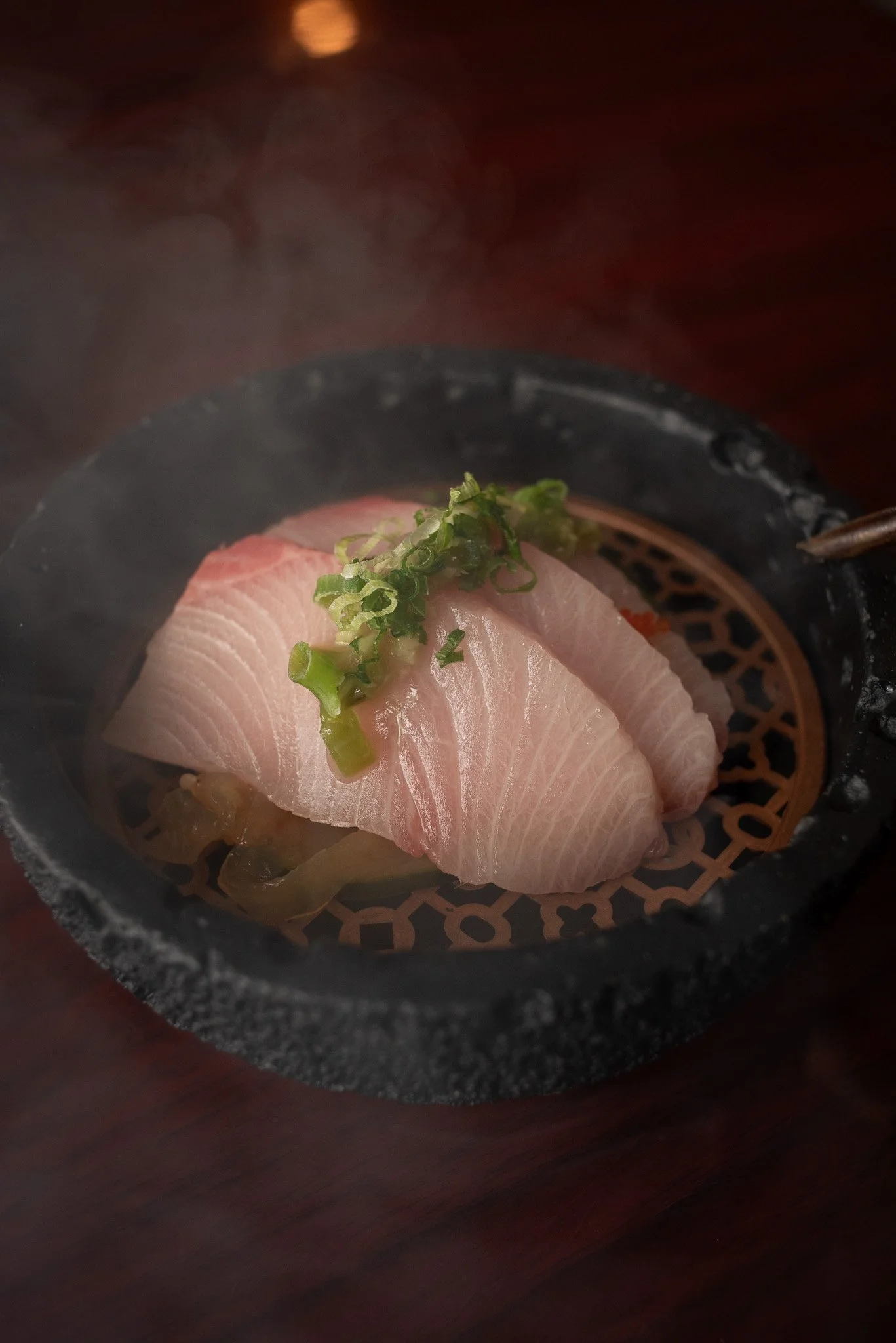 Smoked yellowtail sashimi garnished with chopped green onions, served in a traditional Japanese style.