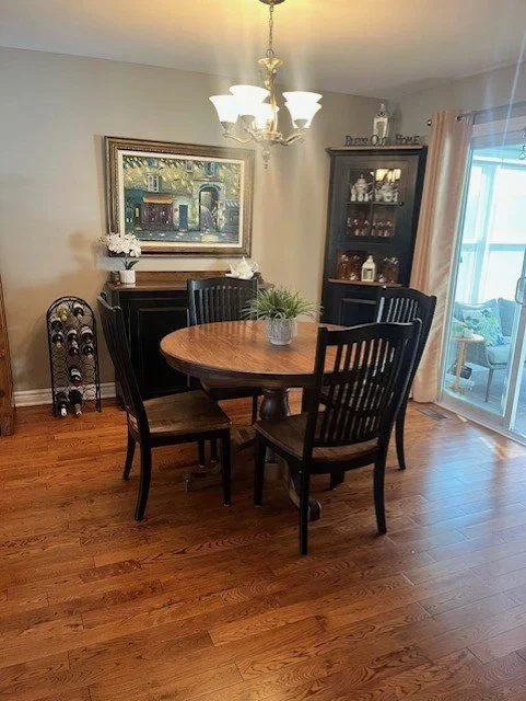 Wooden square table with a pedestal base on a concrete floor, surrounded by various large clock faces on the wall.