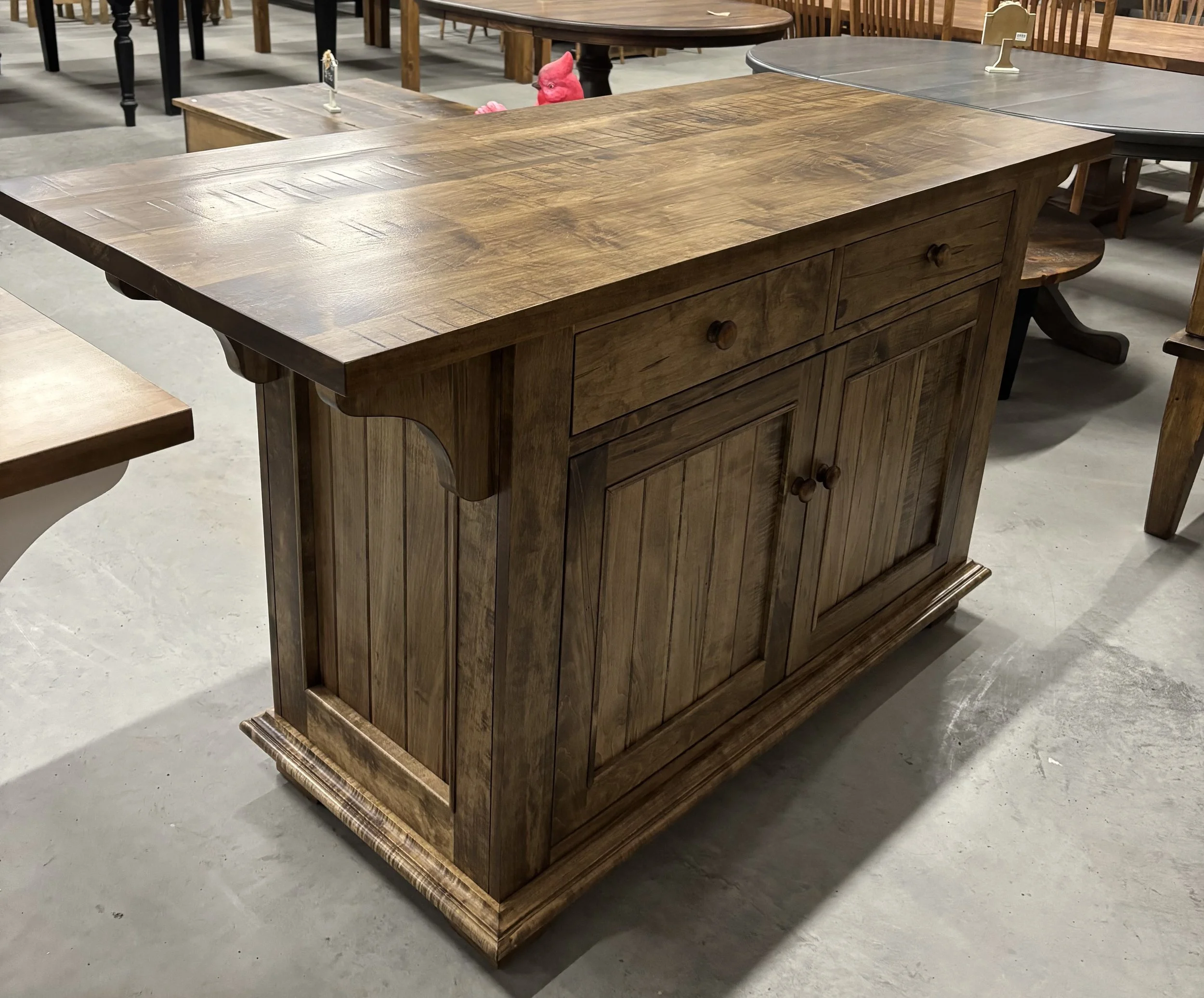 A rustic wooden kitchen island with a dark brown top and an off-white base, featuring a lower shelf for storage, displayed in a showroom.