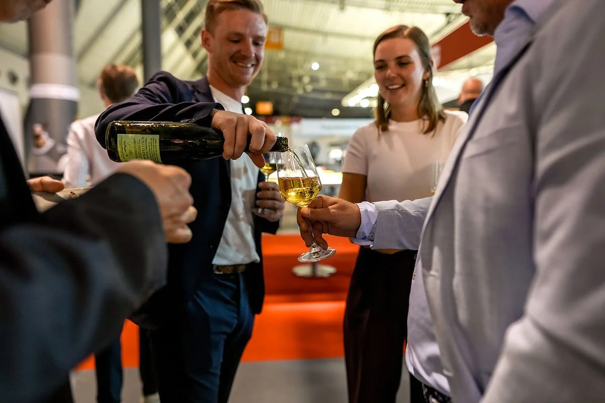 Menschen beim Anstoßen mit Gläsern Weißwein in einer modernen, hell erleuchteten Umgebung.