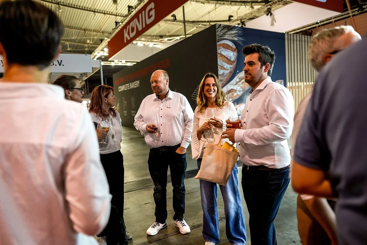 Menschen bei einer Weinprobe auf einer Messe, die lachend und im Gespräch sind.