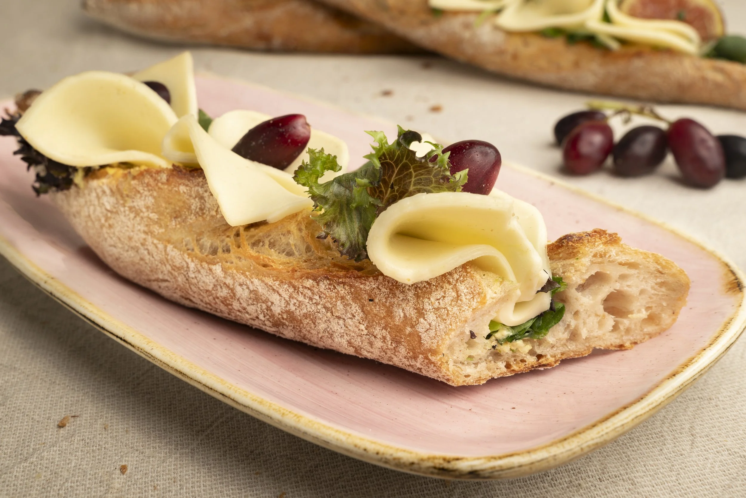 Baguette mit Käse, grünen Blättern, roten Weintrauben und Salat auf einem pinken Teller.