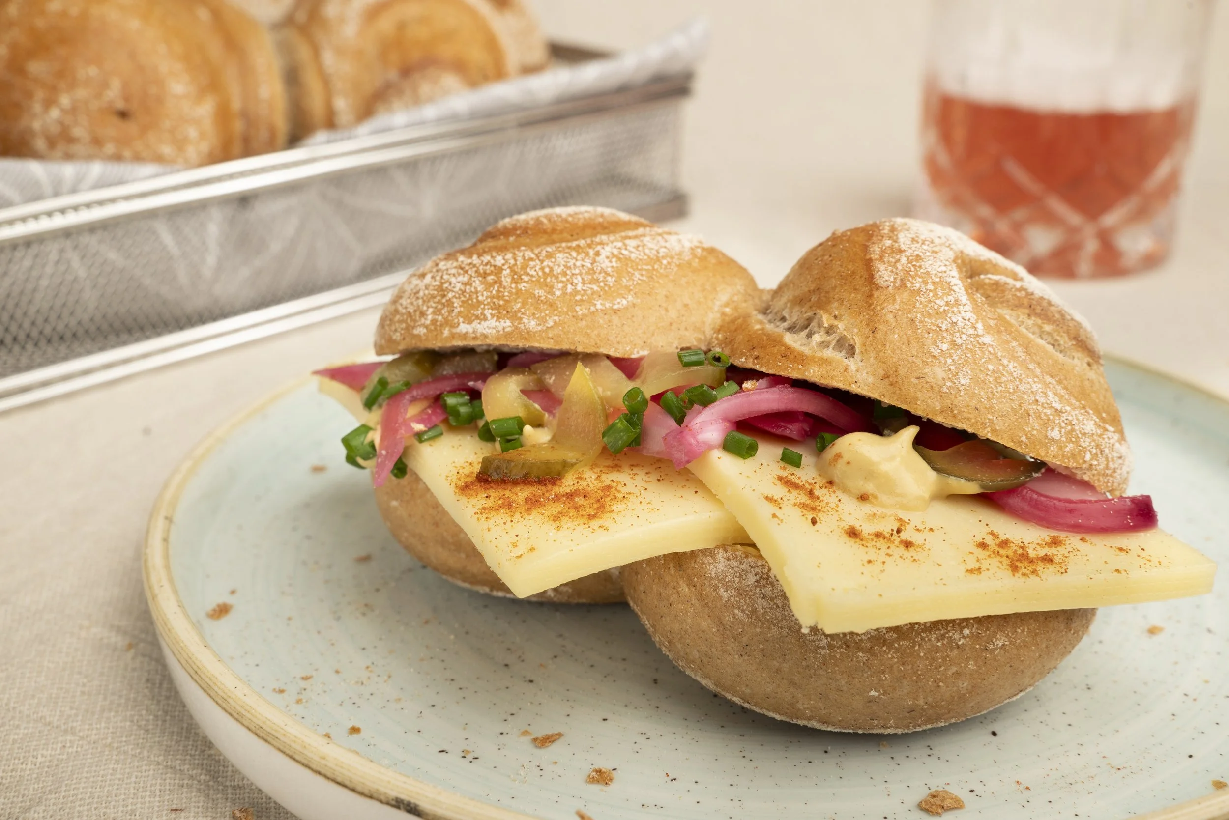 Sandwich mit Käse, Gurken, Zwiebeln und Paprika auf Brötchen, neben einer Glas mit rosa Getränk