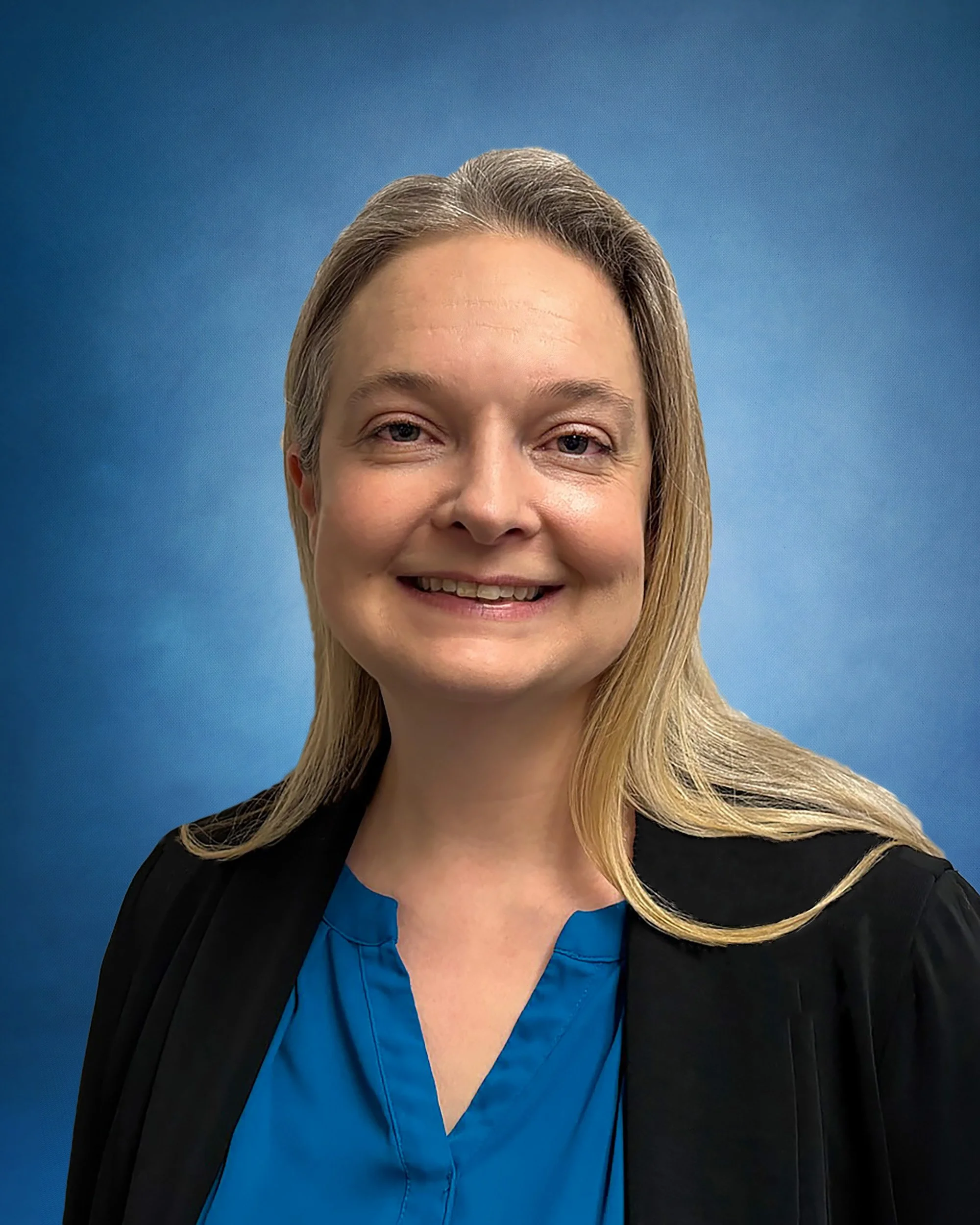 Woman with shoulder length blonde hair smiling with teal shirt and black blazer