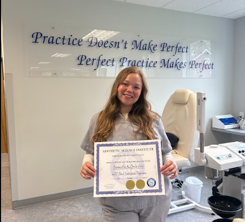 Young woman with long golden blonde hair standing which holding her aesthetician certificate.