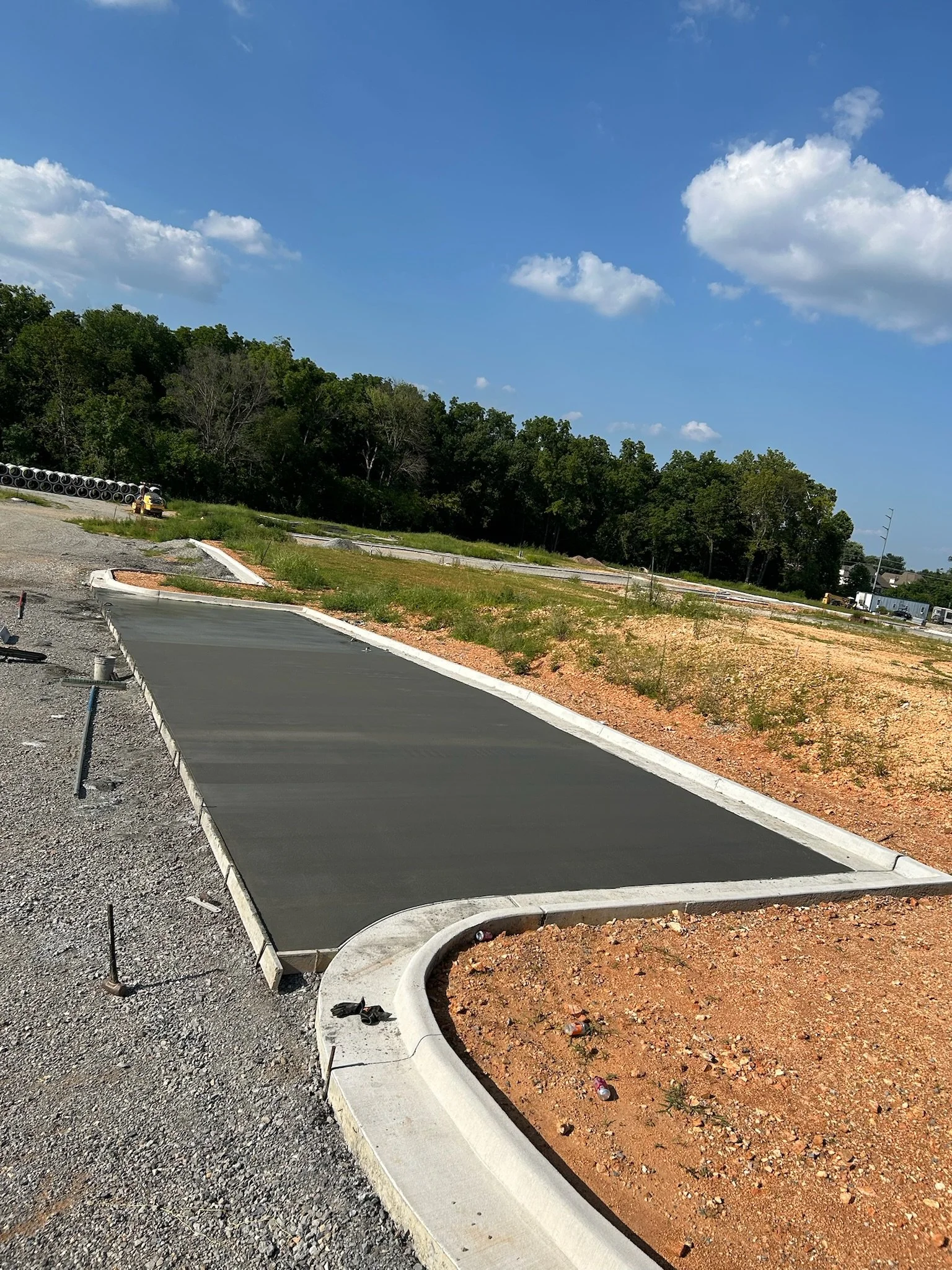 Newly installed dark grey concrete parking bay with finished light grey curbs at the Northwest corner parking area construction site. This view from Phase 1C NW Corner Parking_2.jpg shows smooth concrete placement adjacent to a graded gravel driving 