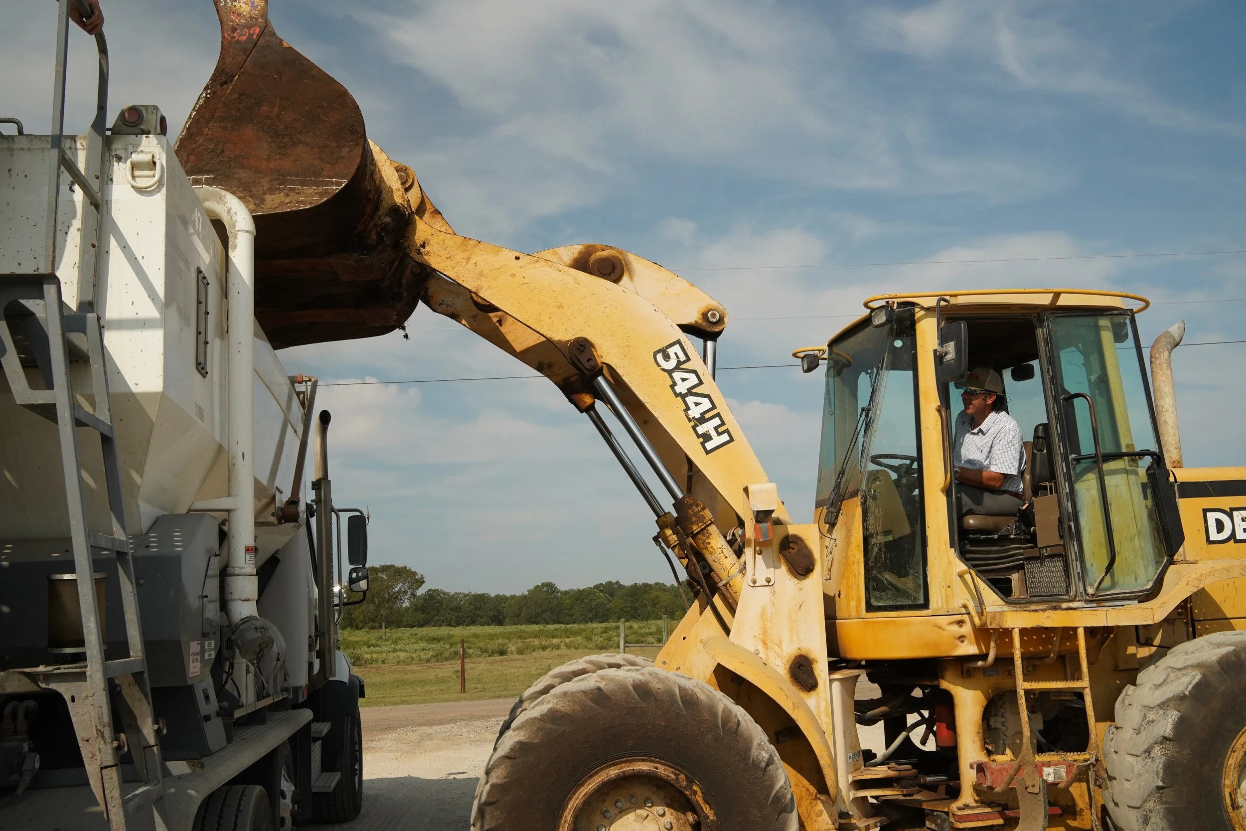 Yellow John Deere wheel loader bucket dispensing dry aggregates at a Sirron industrial job site.