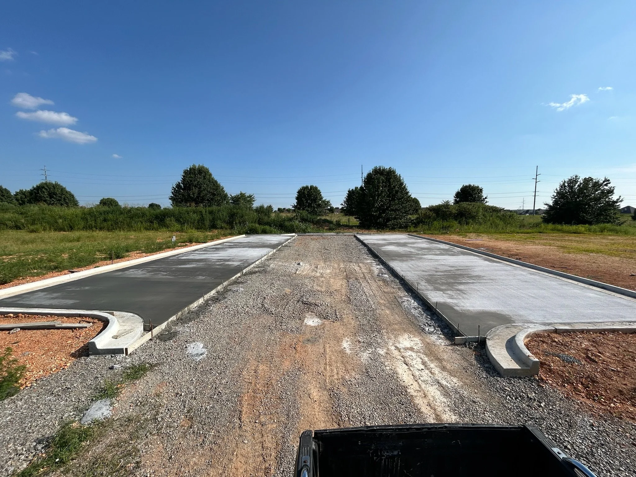 Newly poured concrete parking stalls with concrete curbing in the southwest corner during Phase 1C construction under a clear blue sky.