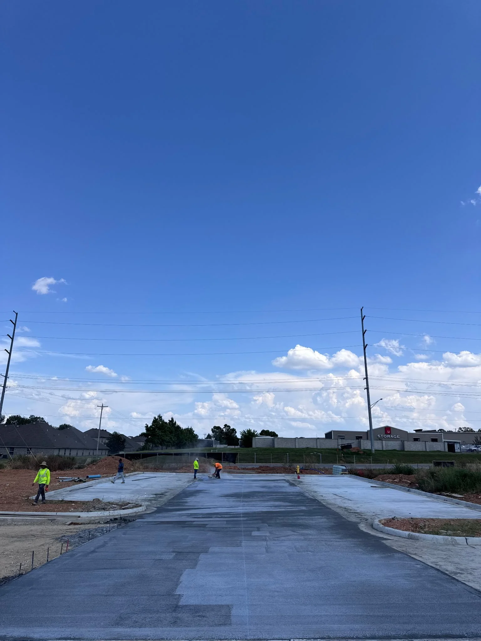 New commercial parking lot construction and paving near a U-Storage facility under a blue sky.