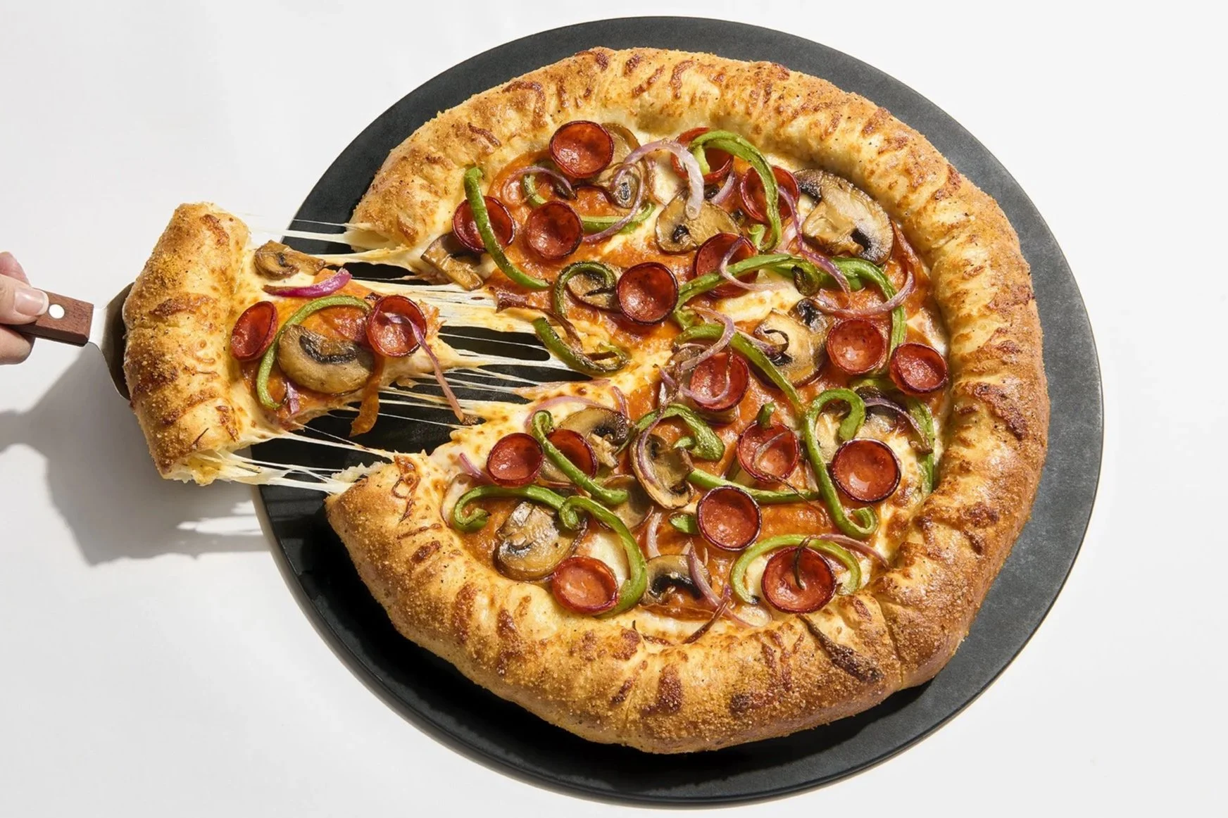 Pizza with pepperoni, green peppers, mushrooms, and onions on a black plate, with a slice being lifted, cheese stretching.