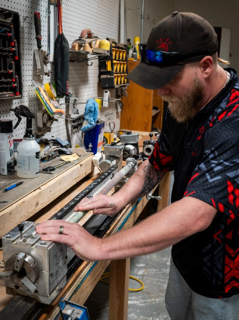 Keith shaping a pool cueon a workshop workbench surrounded by tools and equipment.