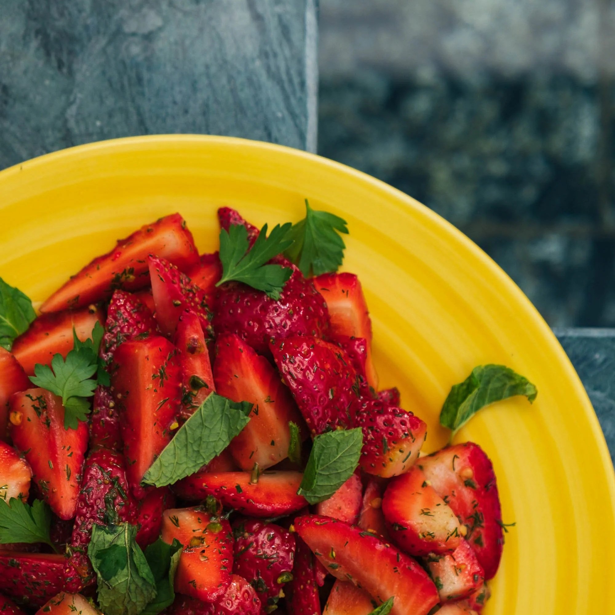 Close-up of a yellow bowl filled with chopped strawberries garnished with fresh mint leaves.