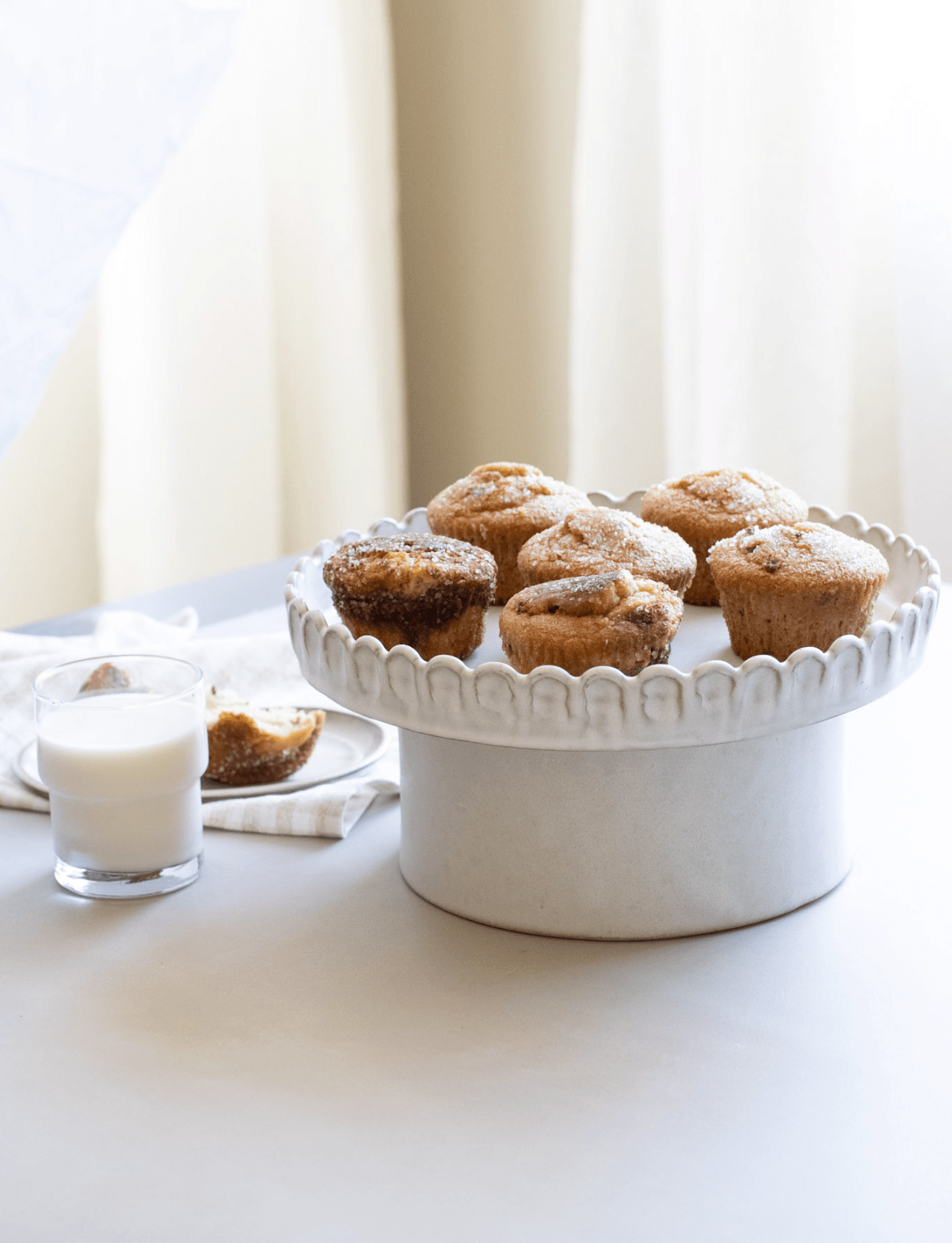 Cinnamon sugar gluten free muffins with a glass of milk on a ceramic cake stand