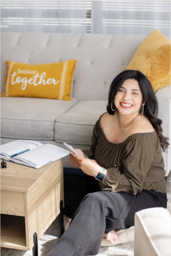 Hispanic woman smiling with brown off the shoulder top on floor in front of tan couch