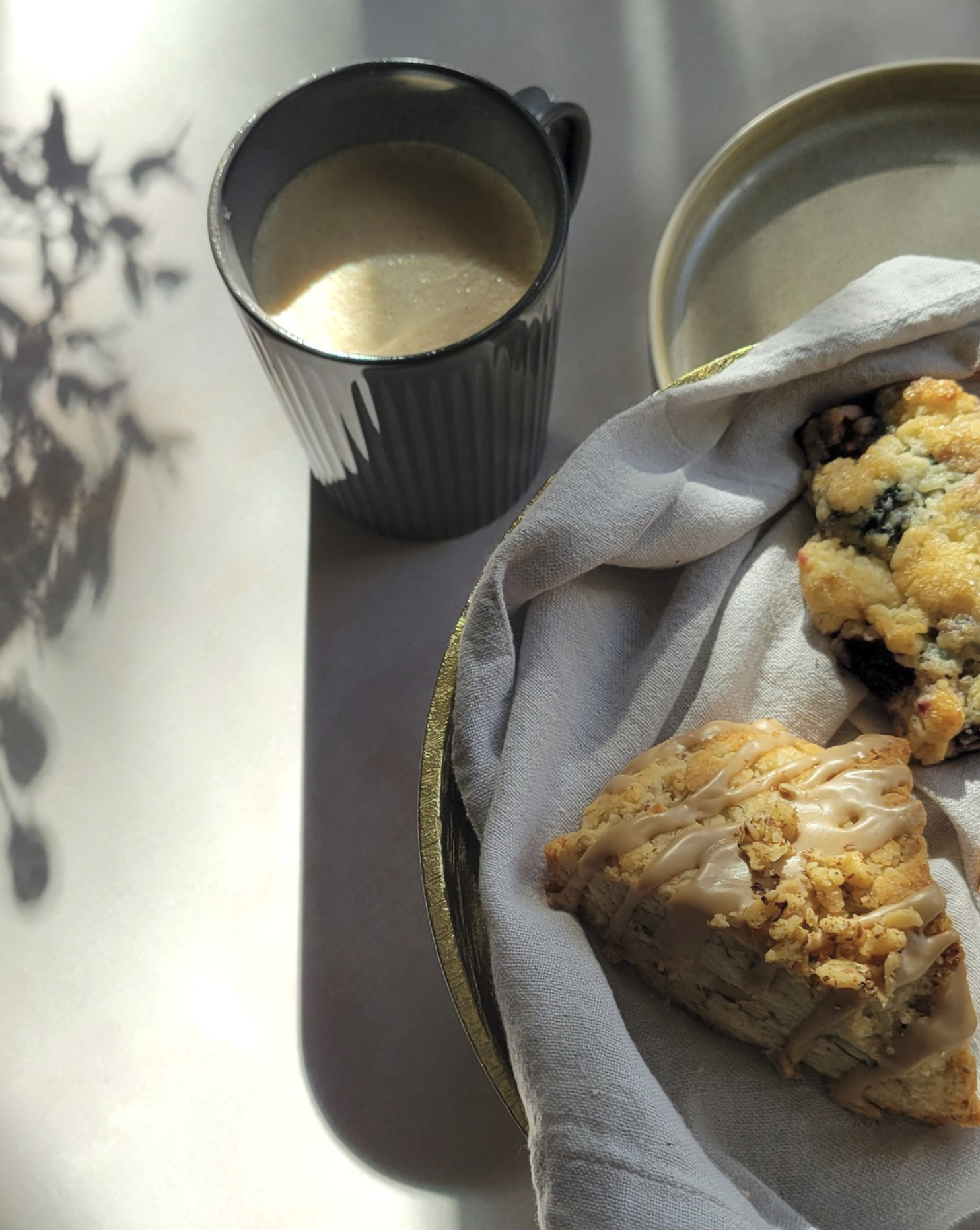 Cup of coffee in blue mug with morning shadows on breakfast table with scones