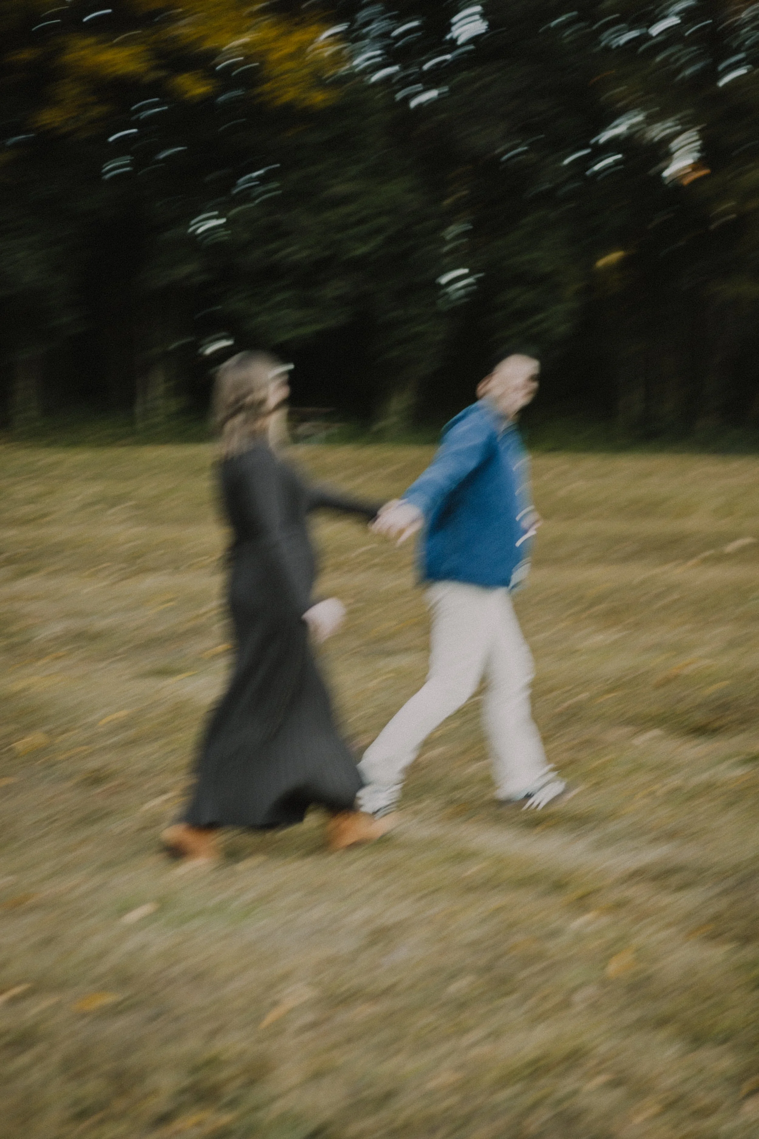 A blurry photo of a couple walking outdoors, holding hands, with trees in the background at dusk or evening.