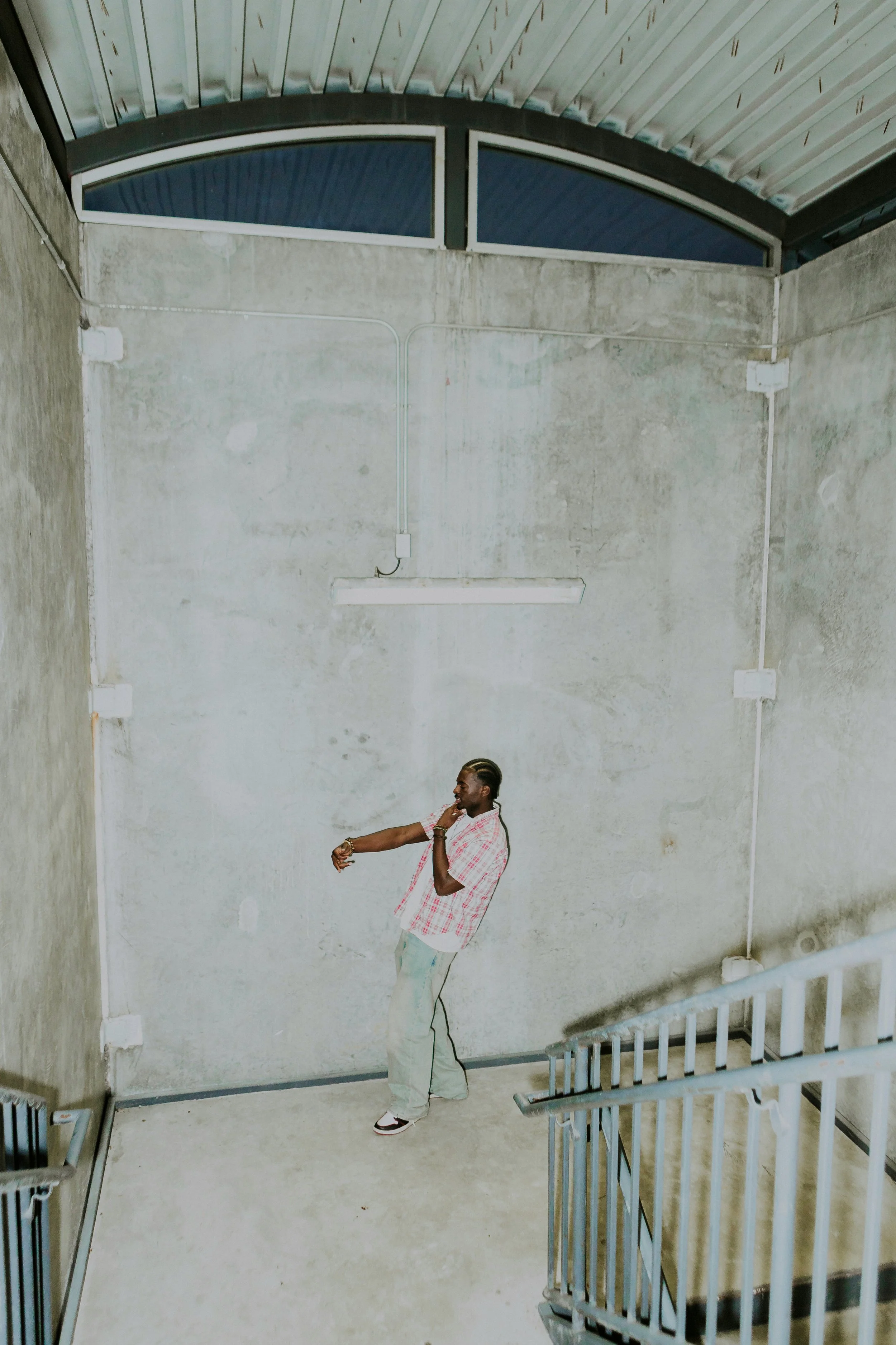 A person dancing in an industrial-style space with concrete walls, metal staircase, and a curved ceiling with skylights.