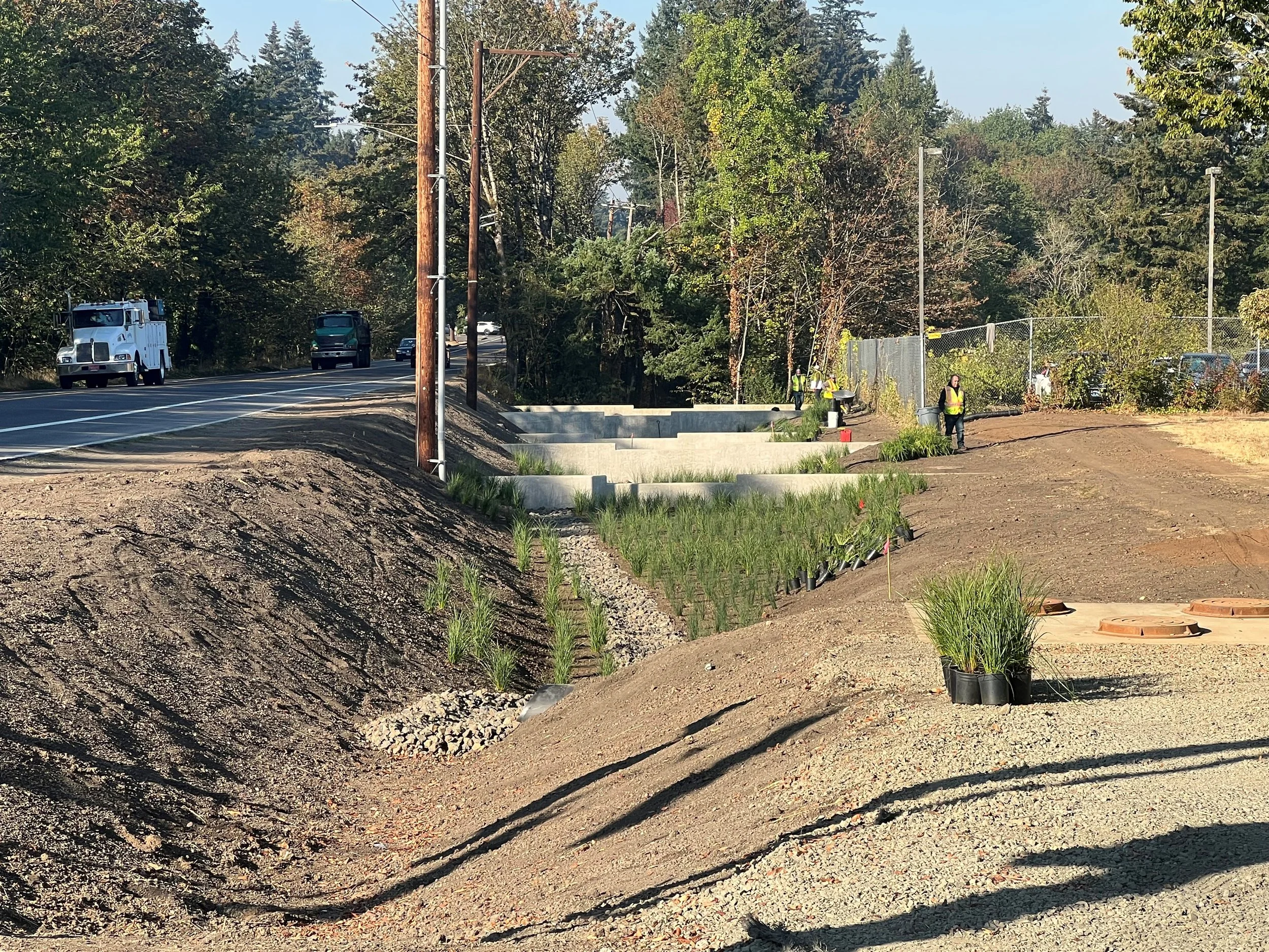 Construction workers planting grass and landscaping along road under clear sky.