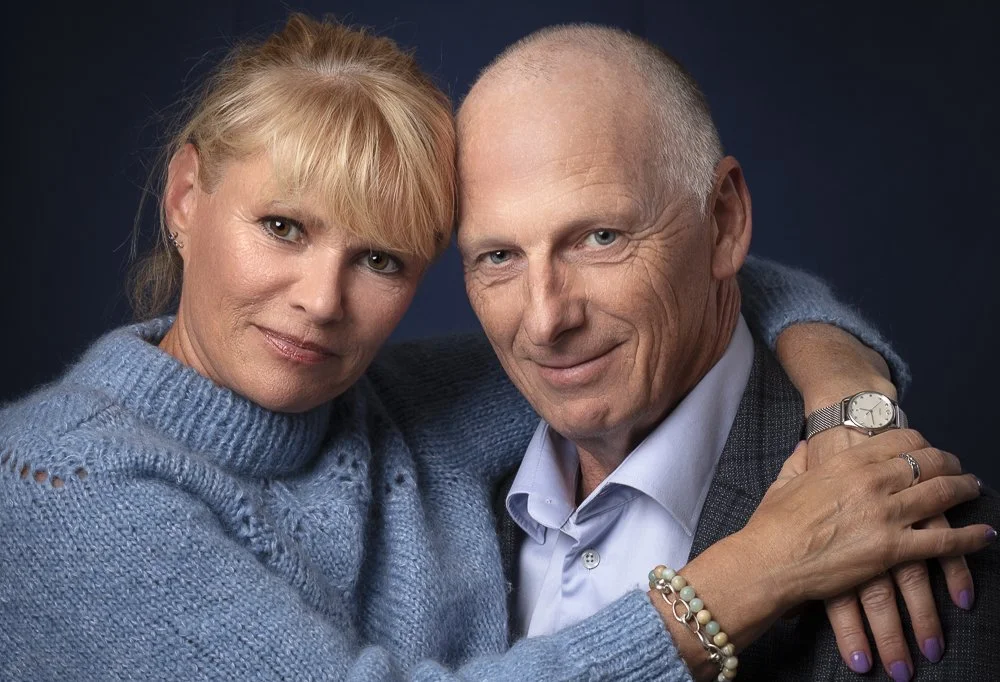 Et par, en kvinde og en mand, poserer tæt sammen mod en mørk baggrund.