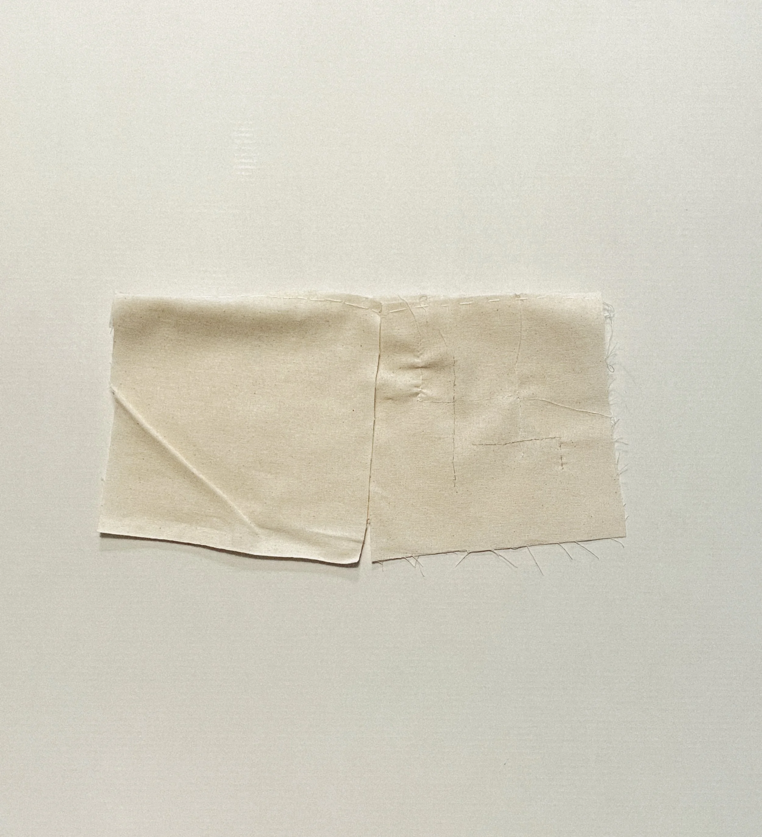 Folded textile work in pale fabric photographed in an open configuration.