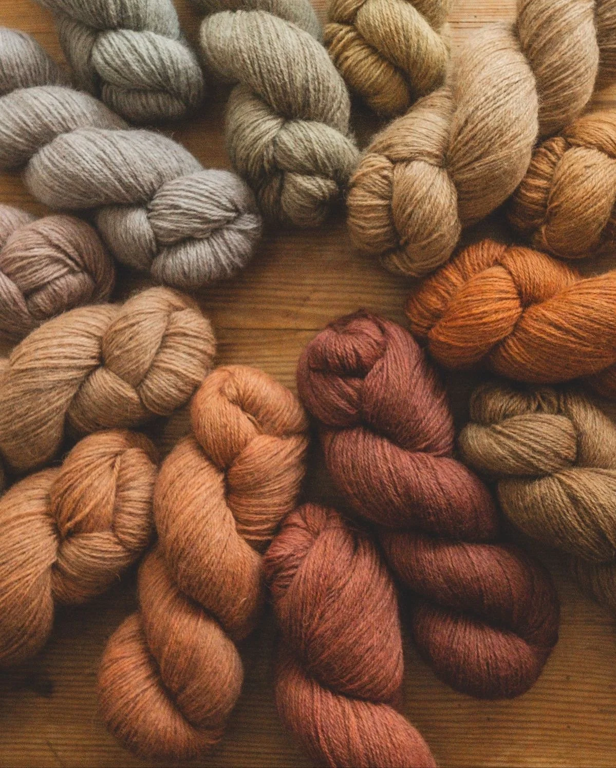 Various skeins of yarn in neutral and earthy tones resting on a wooden surface.