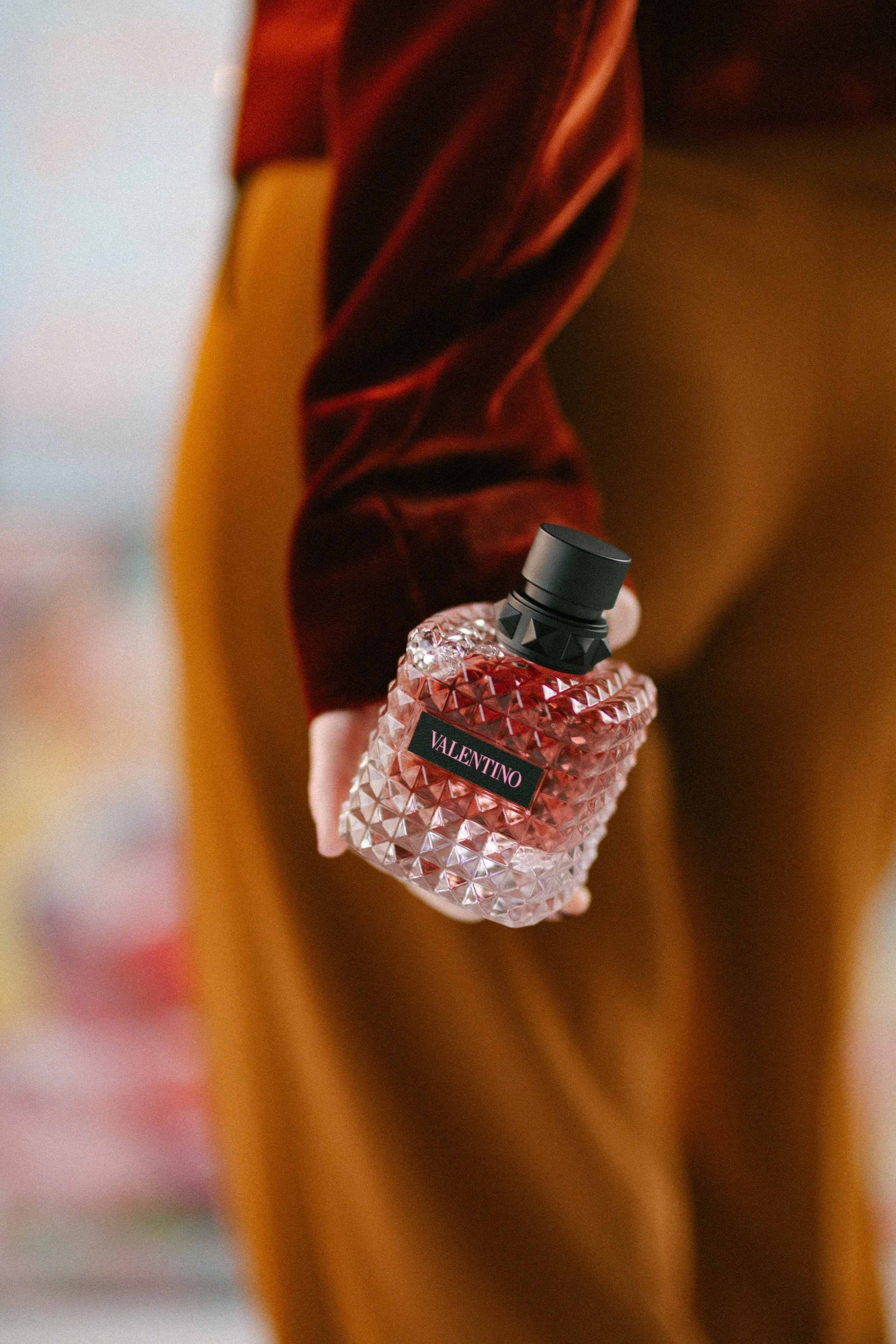 Valentino perfume held in hand with velvet textures and warm colors