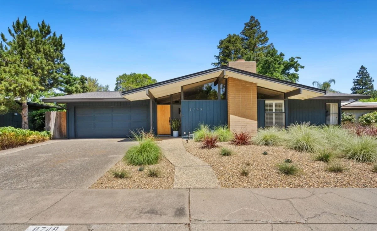 Blue mid century modern Streng Bris home. Gravel garden landscaping. Sand colored brick fireplace.