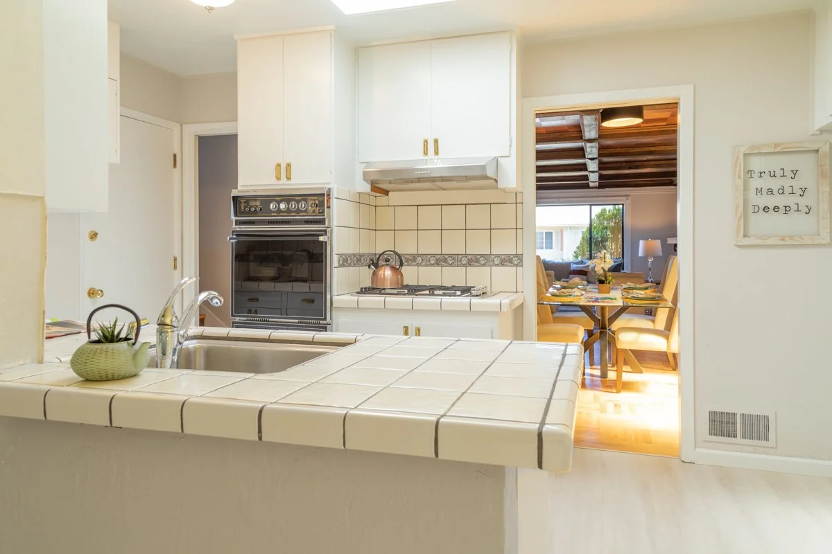 Kitchen with white tile counters with view into dining room. 