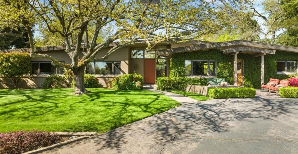 Large Mid Century Modern house with Orange front door. Oak tree in front yard.