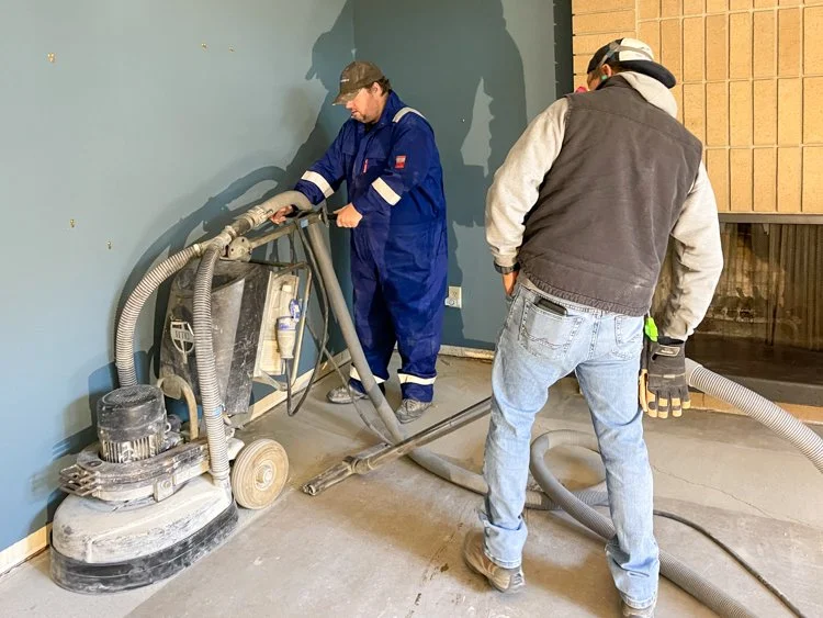Two men grinding a concrete floor.