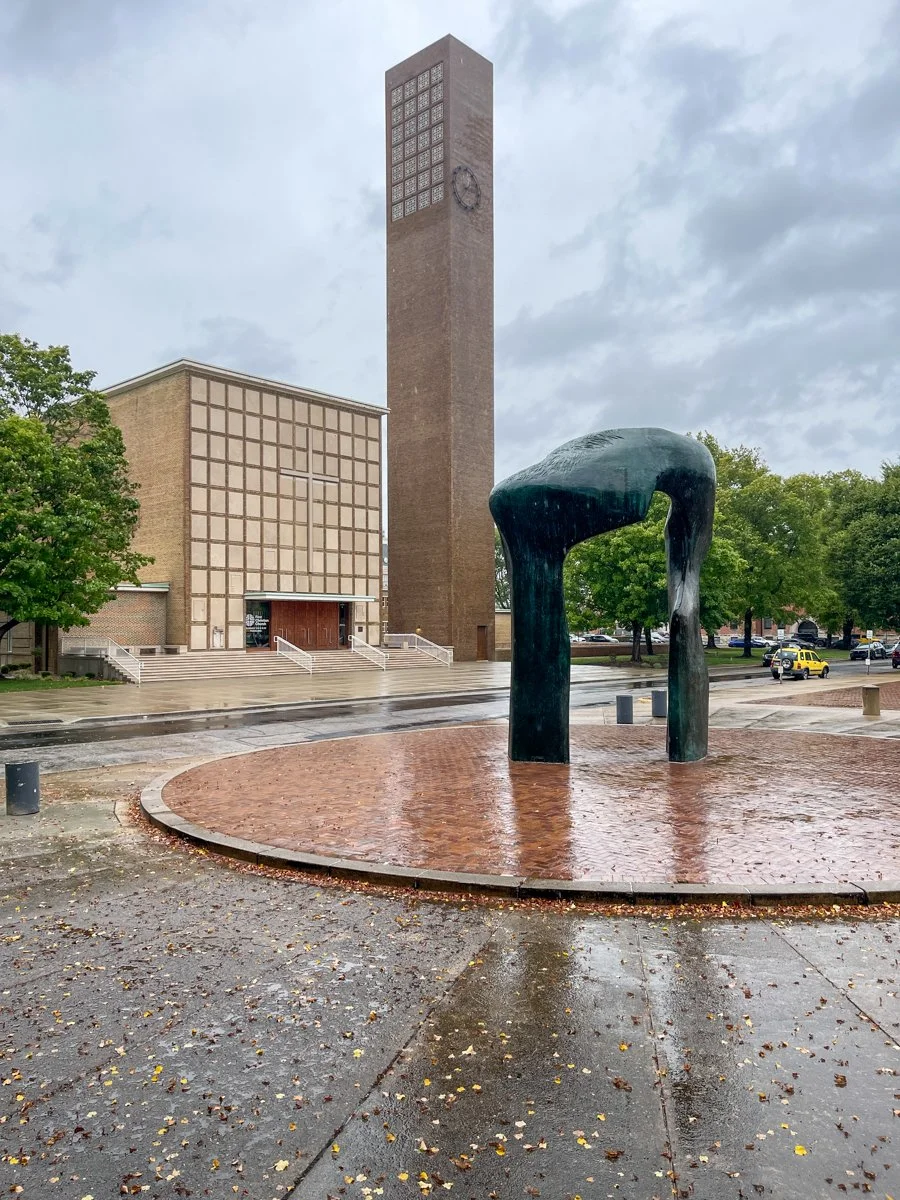 Mid century church with square spire and modern sculpture in front.