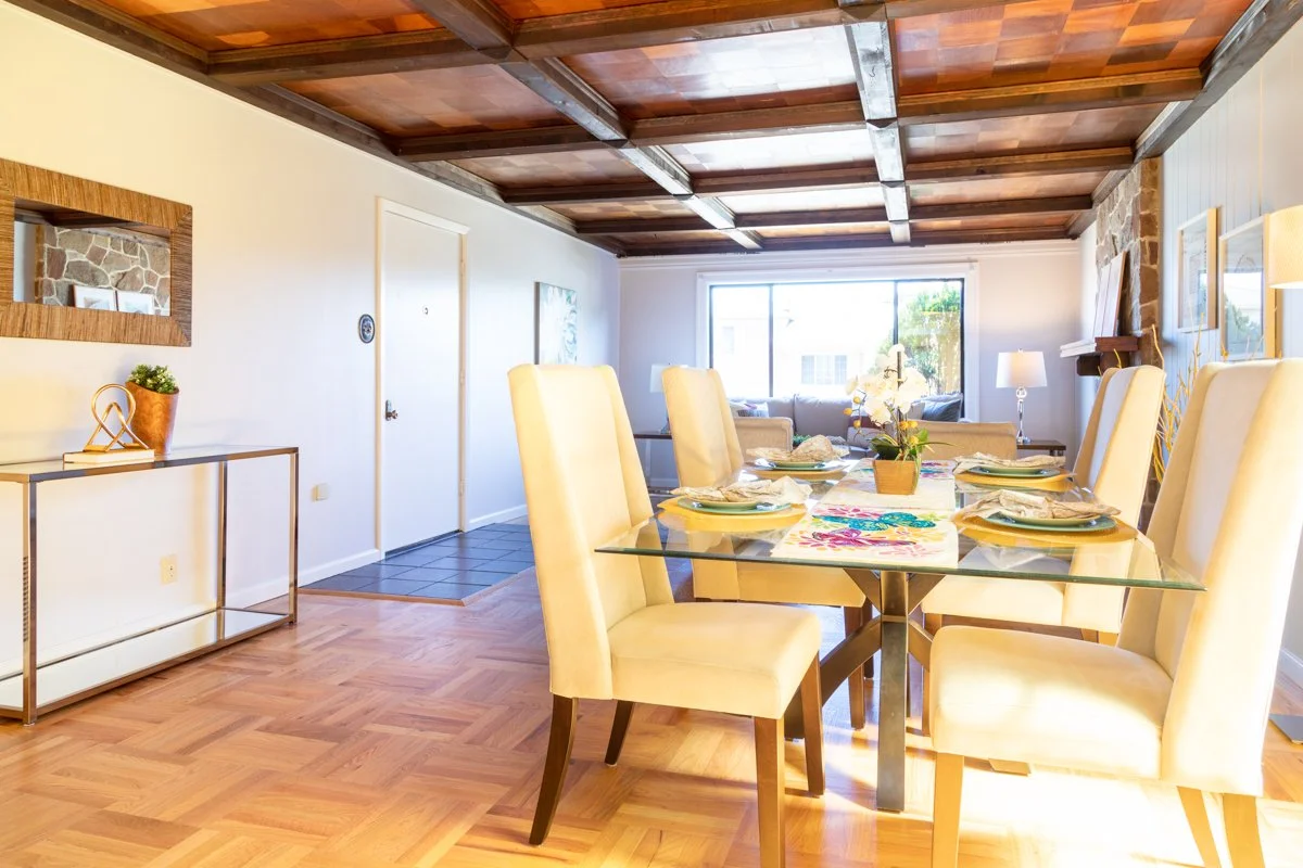 Dining area with living room in background. Wood floors and coffered ceilings.