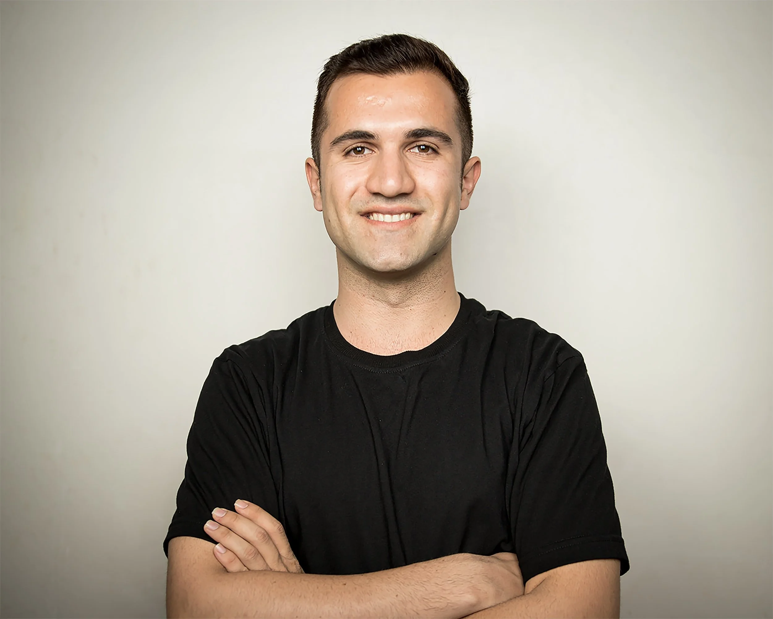 Man in a black t-shirt standing with folded arms, smiling at the camera.