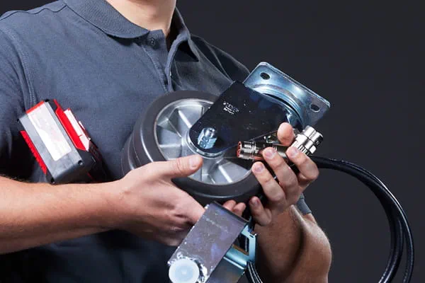 Person holding industrial equipment including a motor, a red and white device, and a rectangular metal component.