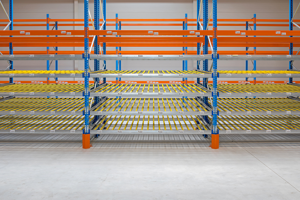 Empty industrial warehouse shelving unit with orange and blue metal framework and yellow rollers, in a storage facility.