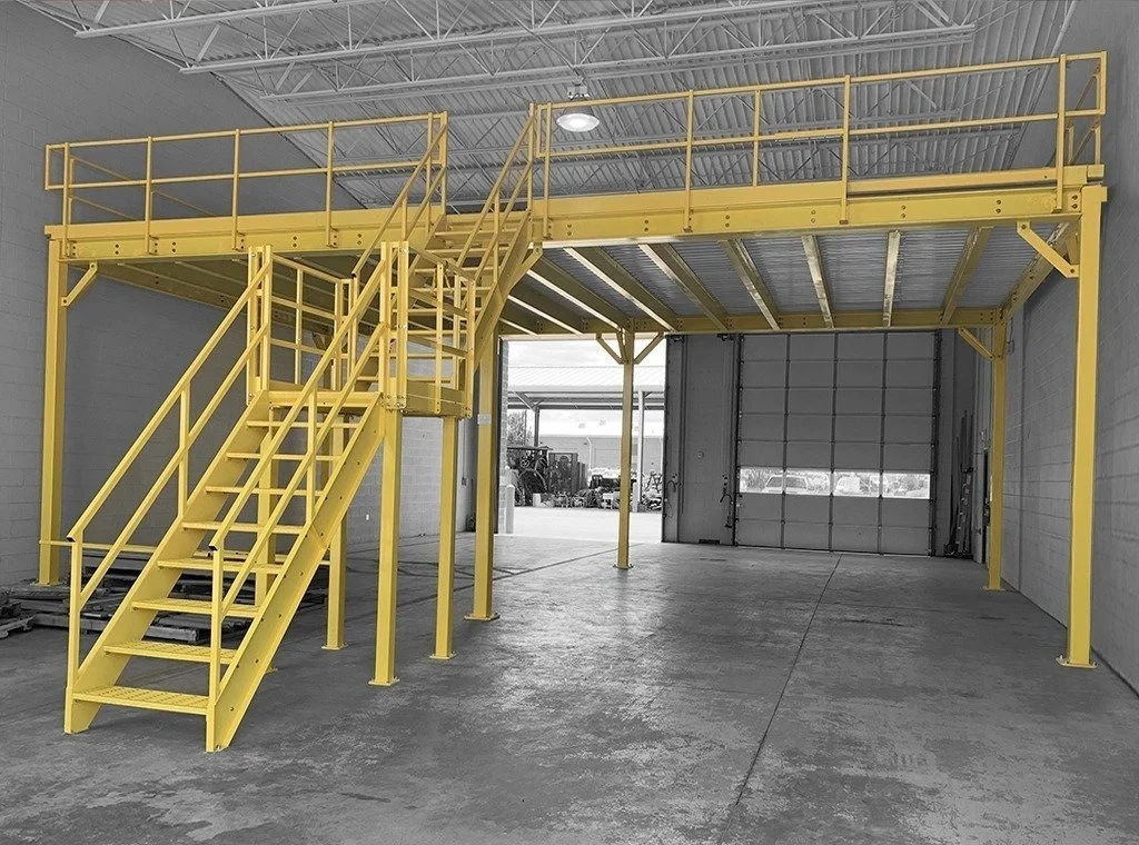 Interior of a manufacturing or industrial facility with metal stairs, ladders, and equipment, and three people working or inspecting in the background.