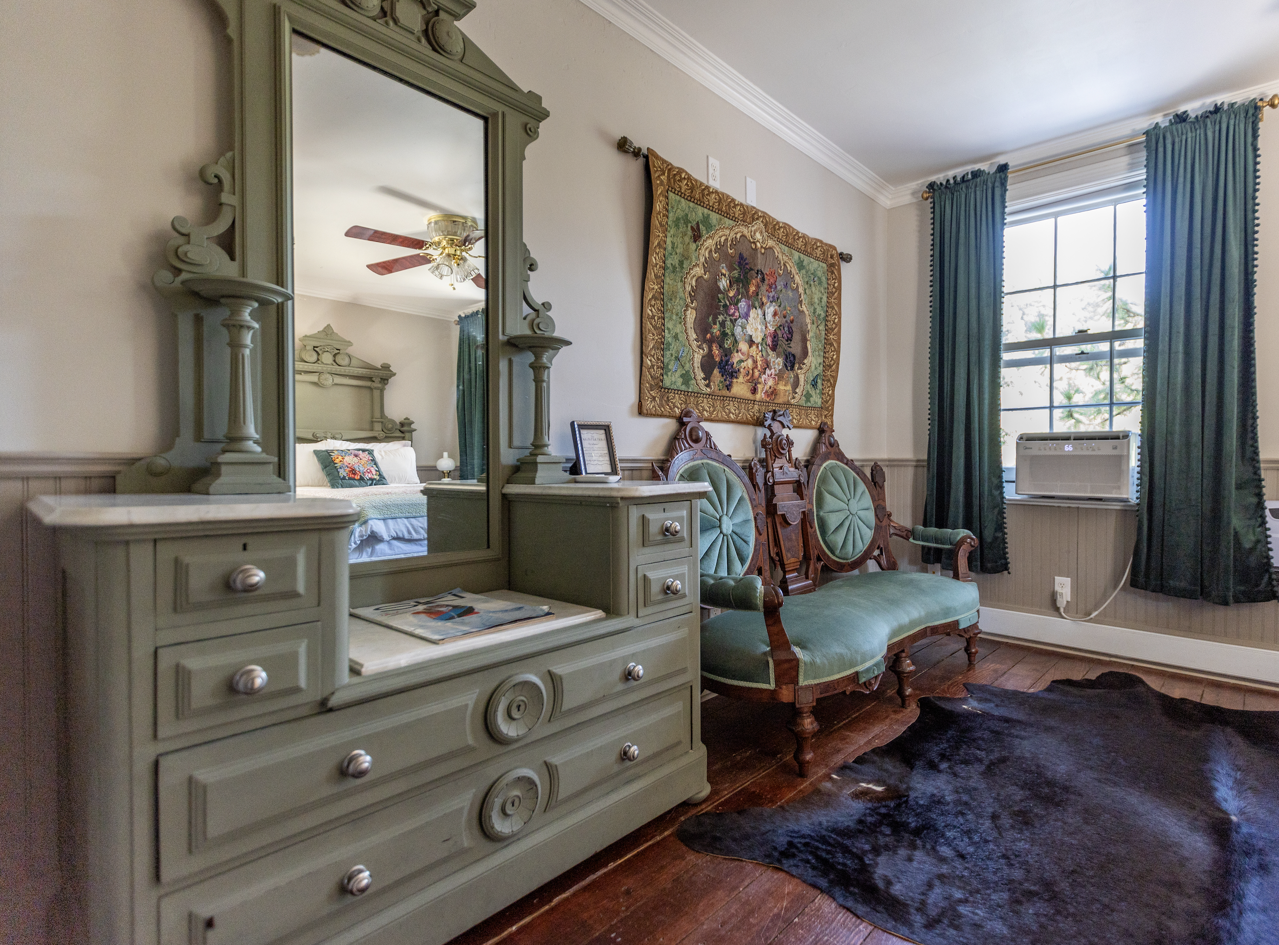 Traditional bedroom with green curtains, wooden furniture, and a ceiling fan