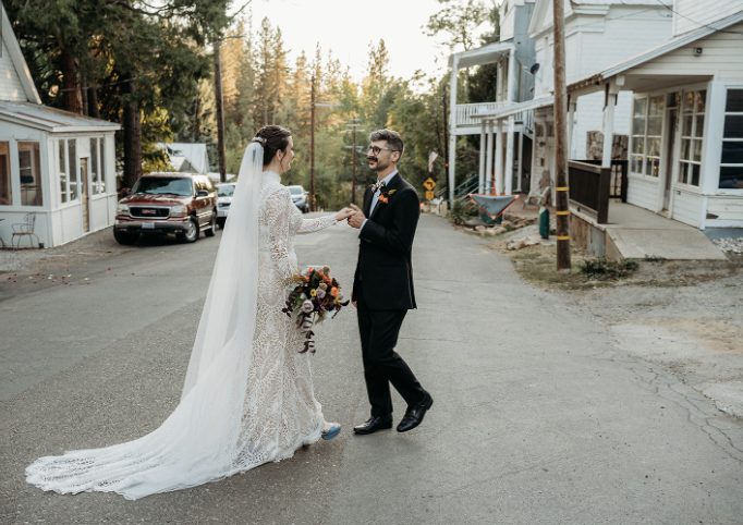 Bride and groom holding hands in the middle of a street, surrounded by houses and trees, celebrating their wedding day.