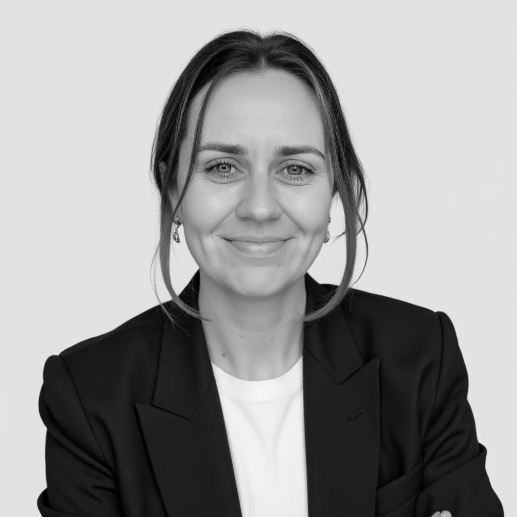 Black and white portrait of a smiling woman with light eyes, wearing a black blazer and earrings, against a plain background.