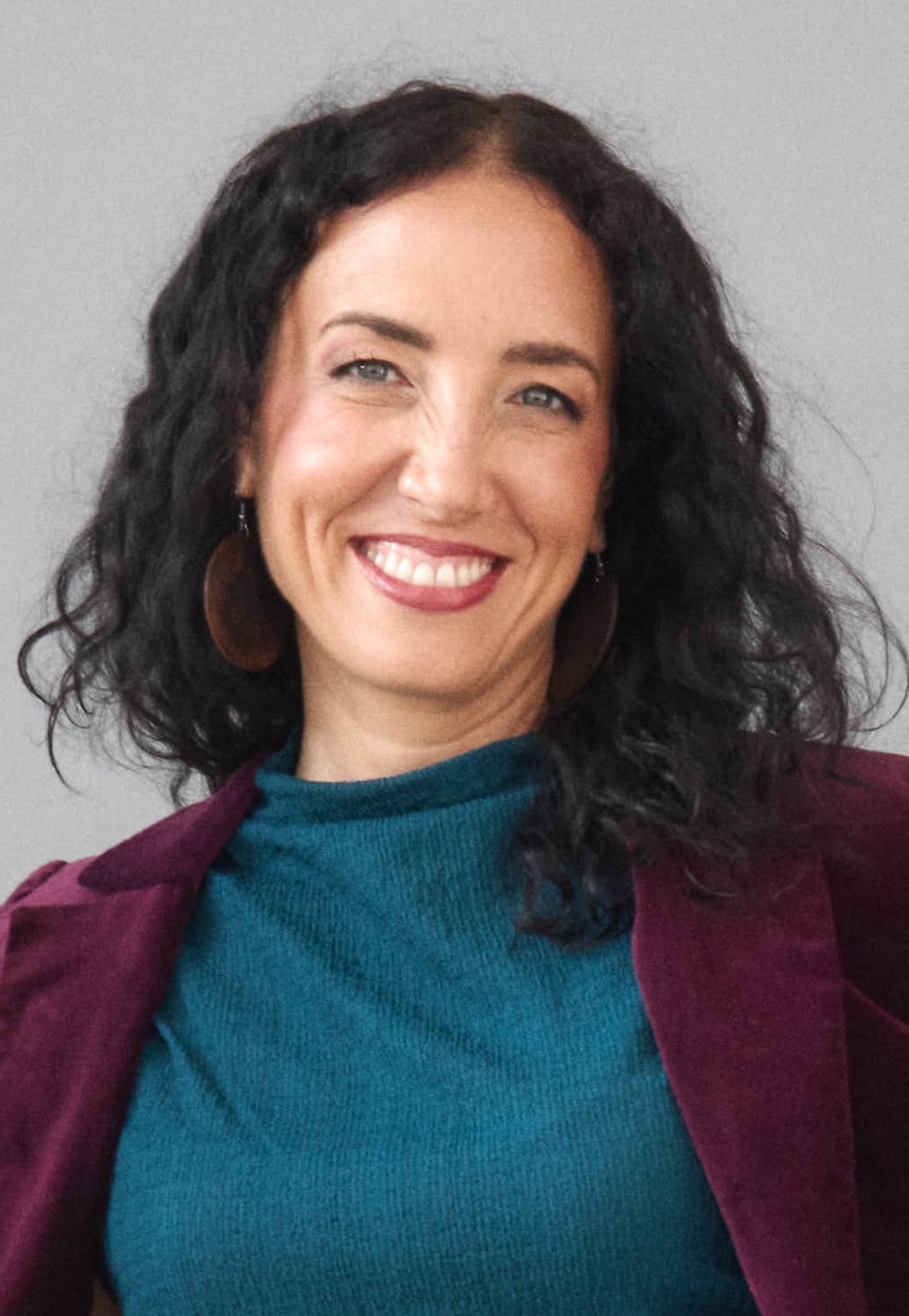 Three dark purple eggplants with green stems on a white plate, accompanied by a purple flower and green leaves.