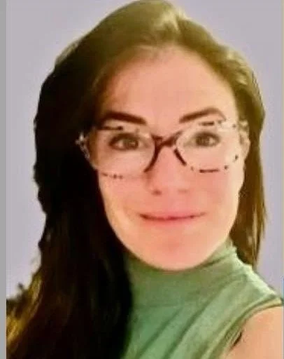A woman with long dark hair wearing glasses and a green top, smiling at the camera.