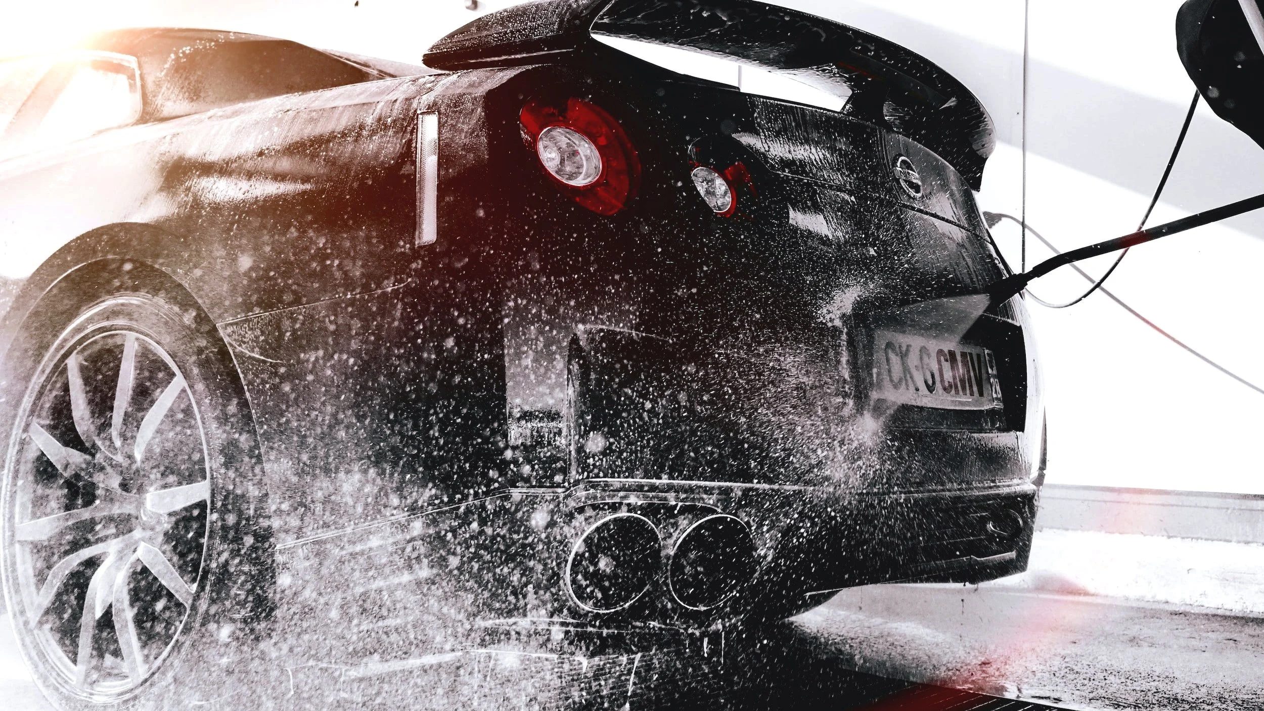 A black sports car undergoing a wash, with water and soap spray visible around it.