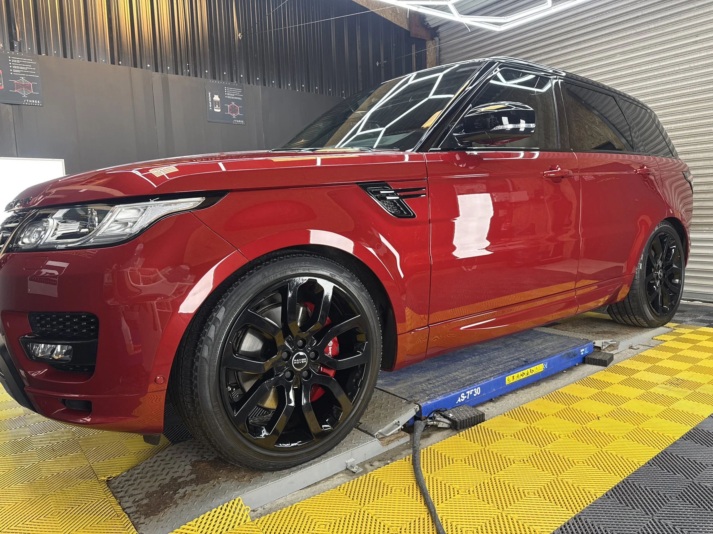 Red luxury SUV with black wheels on a dynamometer testing station inside a garage.
