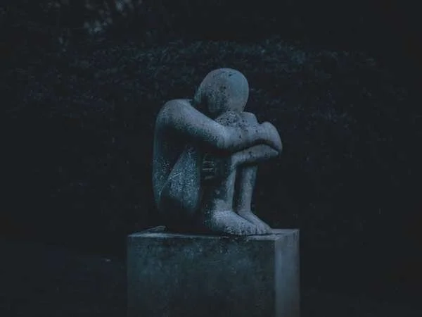 a statue of a person sitting and hugging their knees in to their body
