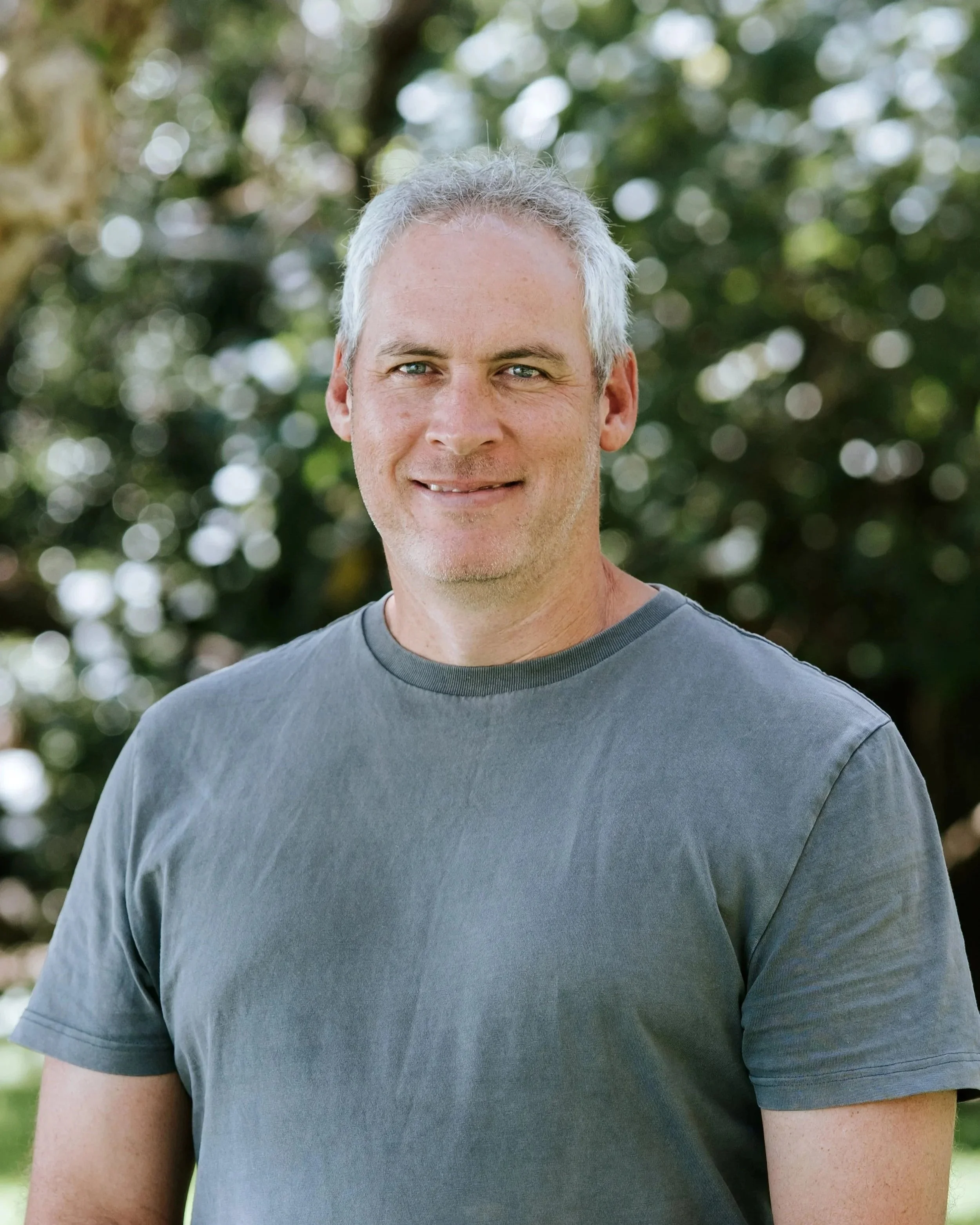 Smiling person standing in front of a lake, wearing a vest with "DCM Building Design" logo.