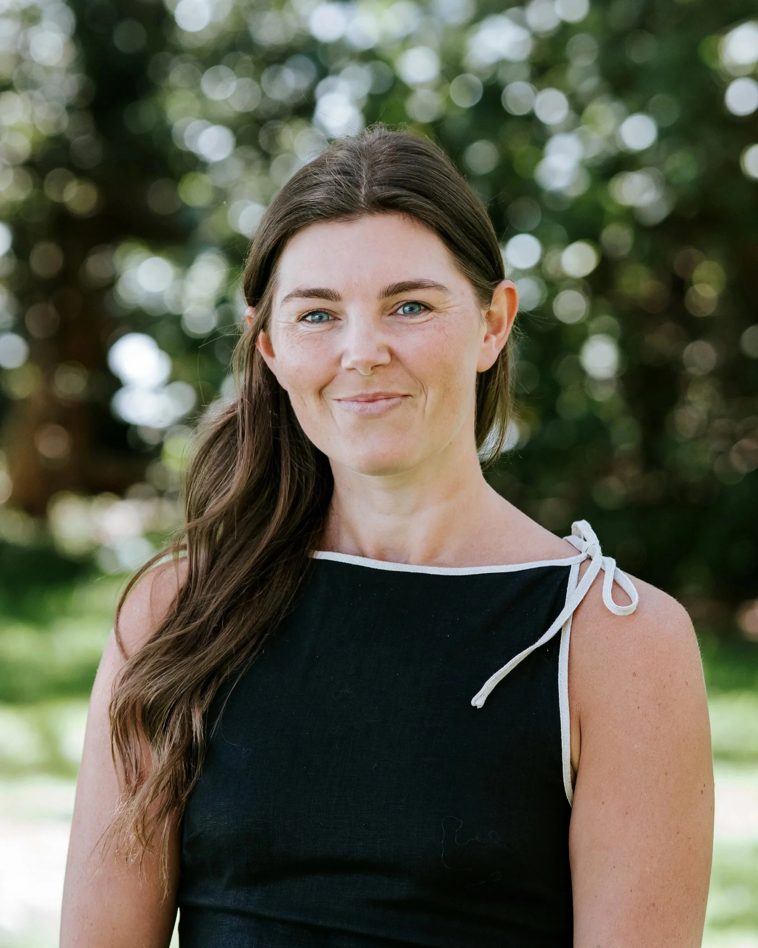 A person with long brown hair wearing a white shirt standing in front of a vertical slatted wooden fence.