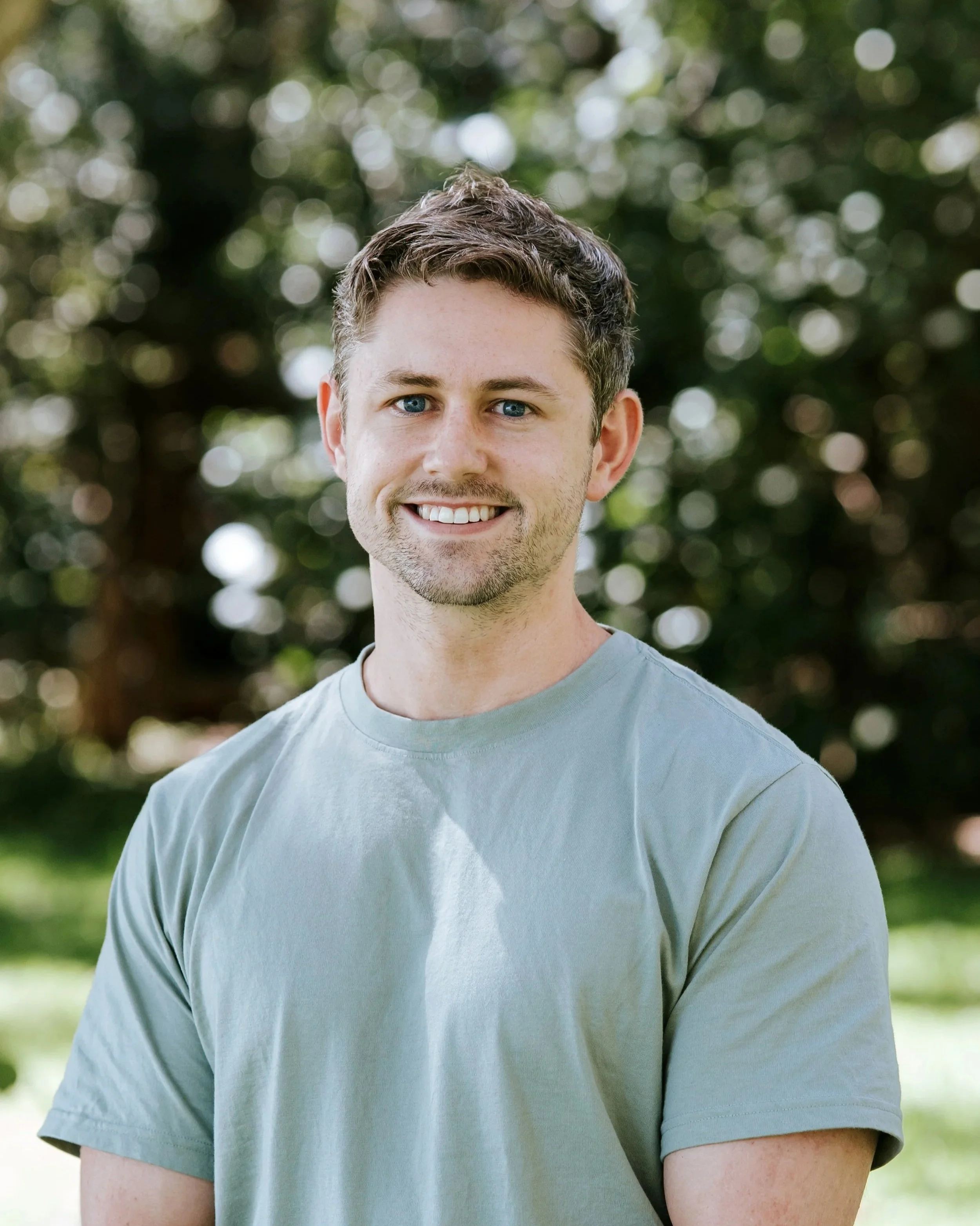 Person in a black shirt standing in front of a wooden slatted wall.