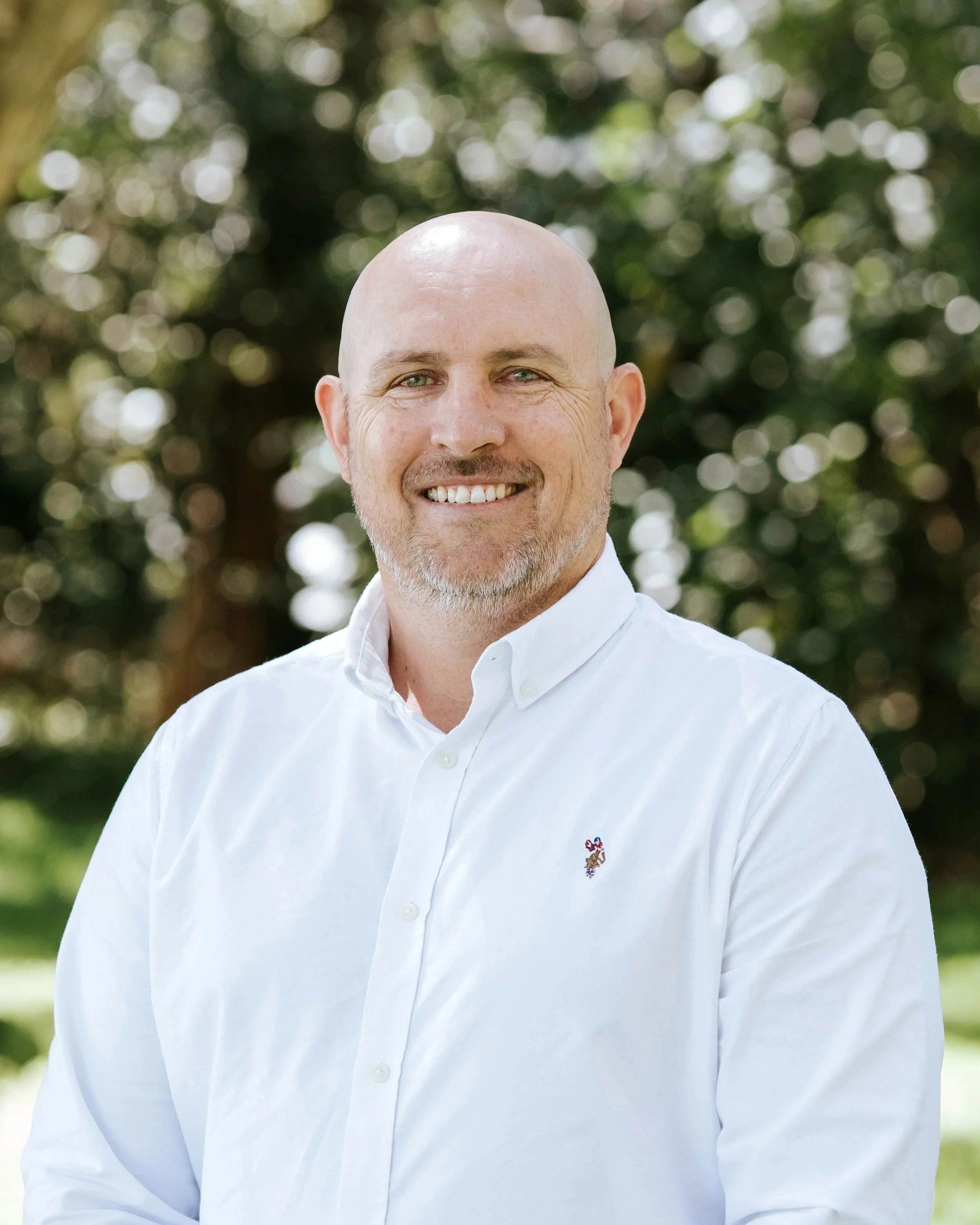 Man wearing black jacket with "DCM" logo standing outdoors near a lake.