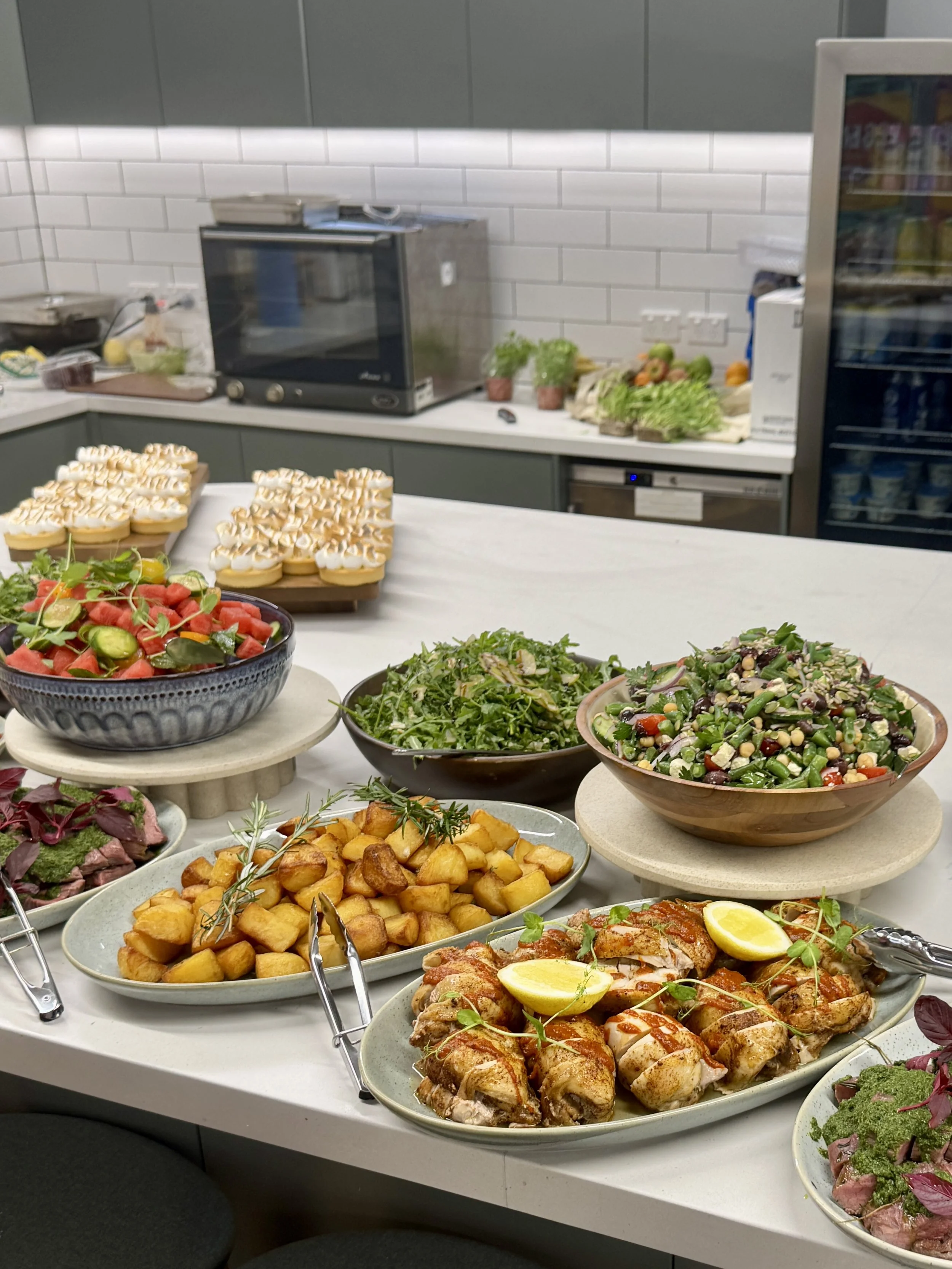 Shared corporate lunch with roast chicken, potatoes and fresh salads set up in an office kitchen