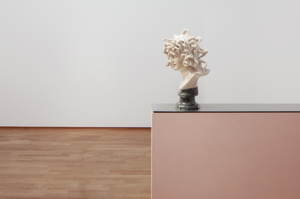A white marble bust of a woman with wild, curly hair displayed on a pedestal in an art gallery